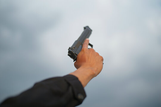 Hand holding a black pistol skyward against a cloudy background. Mexico City, Mexico