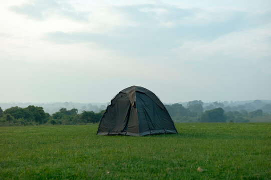 A solitary tent stands on a vast green field under a cloudy sky with distant forests. Ngorongoro Conservation Area, Tanzania