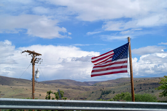 American flag waving on a pole against a vast open landscape and blue sky with clouds. Oregon, USA