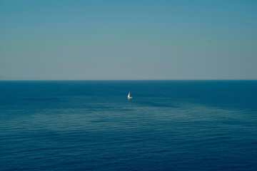 A lone sailboat glides across a calm, vast blue ocean under a clear sky. Peloponnese, Greece