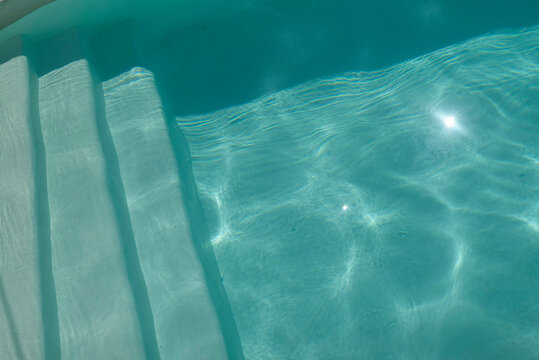 Sunlight refracts in a clear blue swimming pool with visible white steps. Hydra, Greece