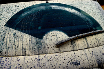 A dirty car windshield with streaks and droplets of dried mud, partially cleaned by a wiper.