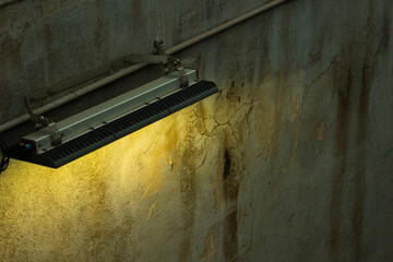 Close up of a lamp illuminating a worn wall in the city, street photography