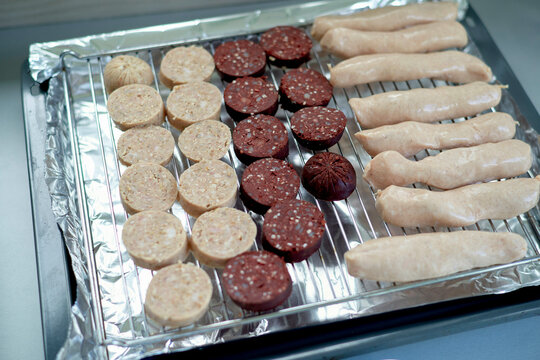 Assorted raw sausages and black pudding on a grill rack with foil lining. Dublin, Ireland
