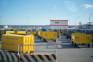 Yellow carts labeled dangerous goods at an industrial area with a building and blue sky.