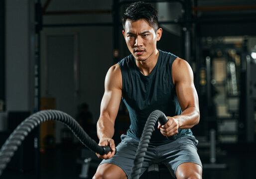 Muscular sportsman exercising with battle ropes during intense cross training at gym