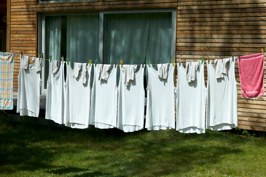 A row of white shirts and towels drying on a clothesline outside a wooden house.