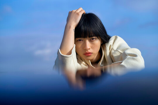 Woman with bangs in white hoodie gazes intently at camera against a clear blue sky. Brandenburg, Germany