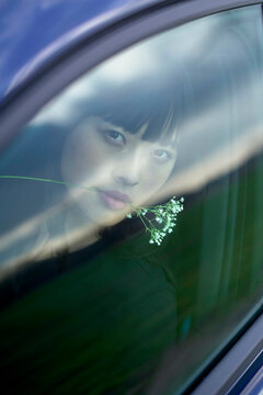 Woman with flowers under her nose gazes out a car window with reflections on glass. Brandenburg, Germany