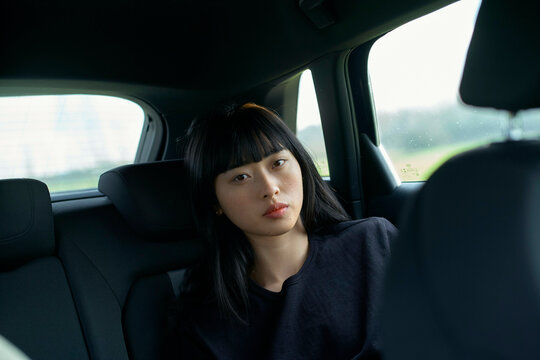 Woman with long black hair sitting in a car's backseat, looking out the window. Brandenburg, Germany
