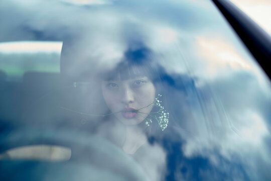 Woman with flowers viewed through car window reflecting blue sky and clouds. Brandenburg, Germany