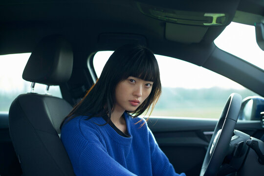 Woman in a blue sweater sits in the driver's seat of a parked car, looking forward. Brandenburg, Germany