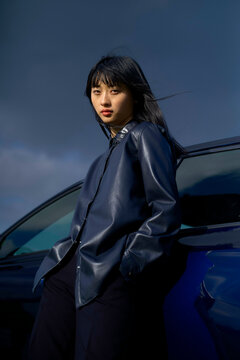Woman in dark blue jacket leaning against a car under a cloudy sky. Brandenburg, Germany