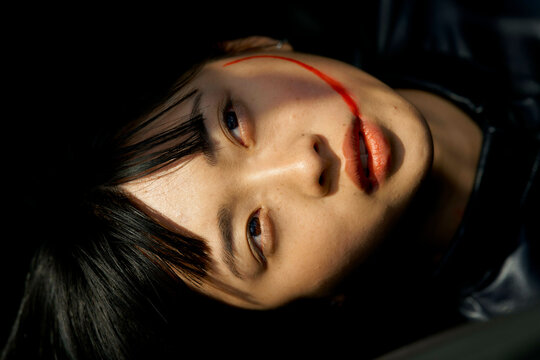 Woman lying down with a red streak across her face, wearing a dark outfit. Brandenburg, Germany