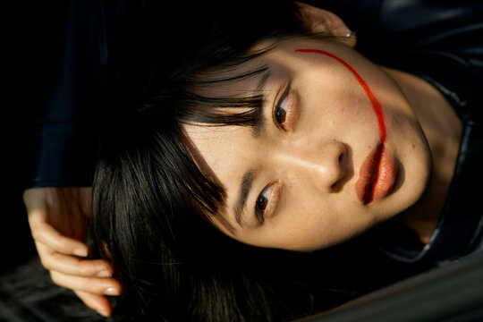 Woman with red makeup line across face lying down with contemplative expression Brandenburg, Germany