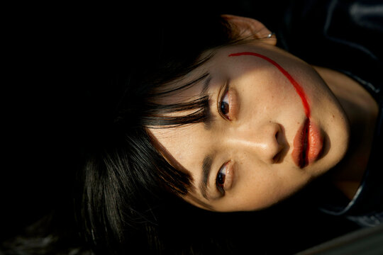 A woman with dark hair and red face paint on her cheek gazes upward against a dark background. Brandenburg, Germany