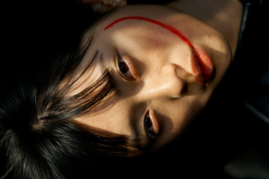 Woman lying with a red streak across her cheek, illuminated by soft light and shadows. Brandenburg, Germany