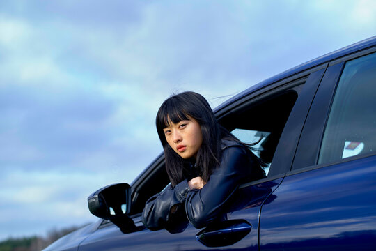 Woman with black hair leans out of a car window, under a cloudy sky. Brandenburg, Germany