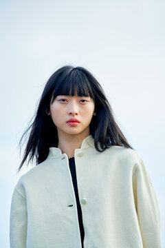 Young woman with long black hair wearing a cream jacket against a clear sky background. Brandenburg, Germany