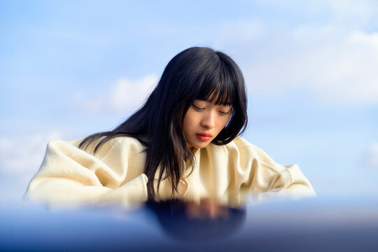 Young woman in a beige sweater looking down against a blue sky background. Brandenburg, Germany
