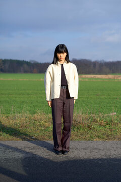 Woman standing on a rural road with green fields and trees in the background. Brandenburg, Germany