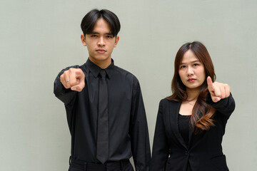 Portrait of young Asian couple wearing business uniform pointing finger at camera