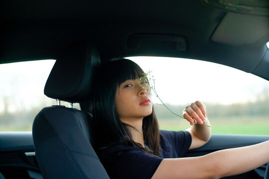Woman sitting in a car holding a flower up to her face. Brandenburg, Germany