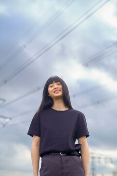 Smiling woman with long hair stands outdoors under a cloudy sky with power lines above. Brandenburg, Germany