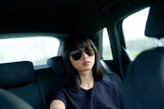 Woman with sunglasses sitting in back of car, looking out window with calm expression. Brandenburg, Germany