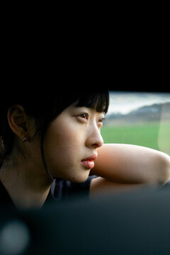 Young woman with thoughtful expression looking out of a car window at the landscape. Brandenburg, Germany