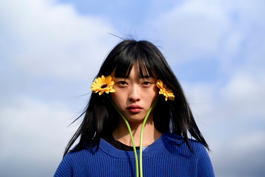 Woman in blue sweater with two yellow flowers framing her face against a cloudy sky. Brandenburg, Germany