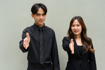 Portrait of young Asian couple wearing business uniform offering handshake