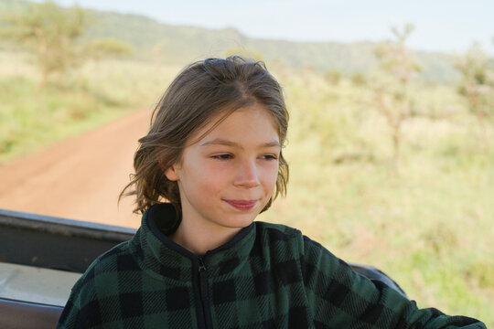 Young boy with brown hair enjoying a safari ride in a grassy landscape under a clear sky. Serengeti, Tanzania