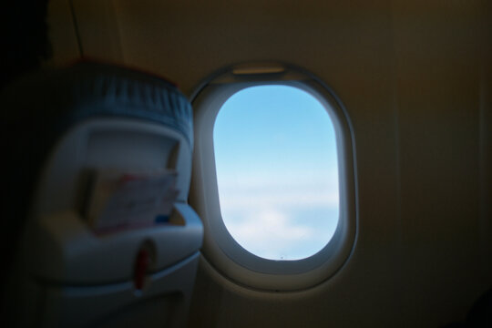 Airplane window view of blue sky and clouds with seatback in foreground.