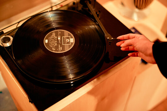 Hand adjusting the tonearm of a vintage turntable with a black vinyl record.