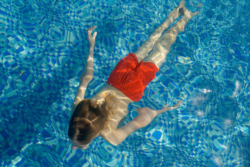 Young boy swimming underwater in a pool with rippling blue water. Tanzania, Africa