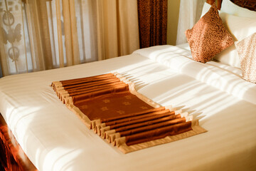 Sunlit hotel bed with folded decorative runner and pillows. Tanzania, Africa