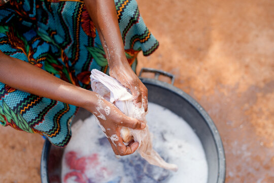 Hands washing clothes in soapy water, wearing colorful patterned fabric, outdoors. Tanzania, Africa