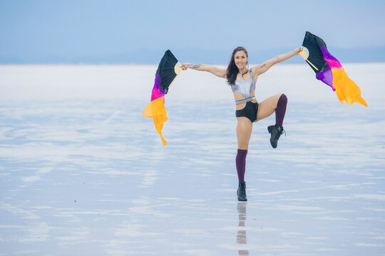 Woman in sporty outfit performs dance with colorful flags on vast salt flat. Bonneville Salt Flats, Utah, USA