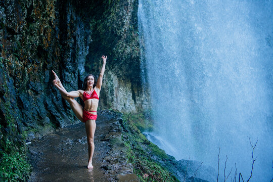 Woman in red athletic wear doing a stretch pose beside a large waterfall. Silver Falls, Oregon, USA