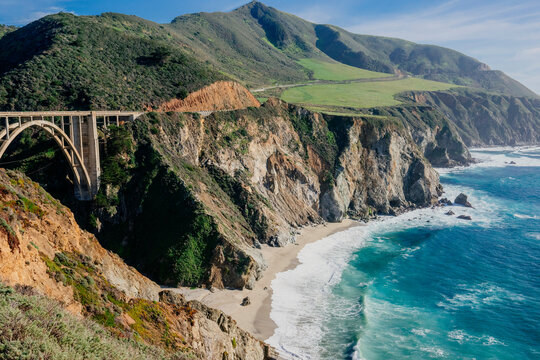 Majestic coastal view with lush hills, rocky cliffs, and the scenic Bixby Creek Bridge over the ocean. California, USA