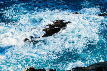 Turbulent ocean waves crashing against rocky cliff under a sunny sky Monterey, CA, USA