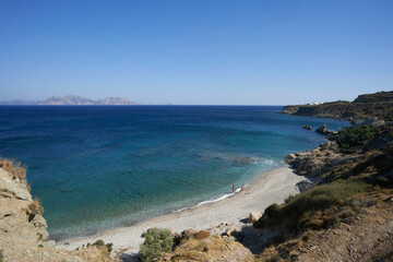 A serene coastline with turquoise waters, rocky cliffs, and a small sandy beach under a clear sky.