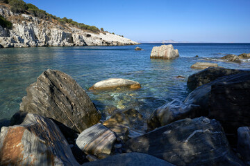 Rocky shore with clear blue water and distant cliffs under a bright sky.