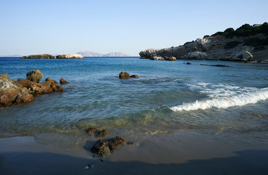 Tranquil ocean waves gently lapping against a rocky beach under a clear blue sky.