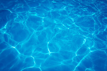 Clear blue swimming pool water surface with sunlight reflections creating abstract patterns and ripples, evoking a refreshing and tranquil summer vibe.