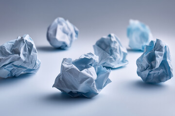 Naklejka premium Close-up of crumpled light-blue paper balls scattered on a pale-blue surface, showcasing texture and form, symbolizing discarded ideas or brainstorming process