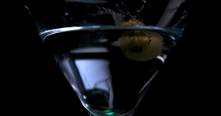 Olive falling into a glass with martini on a black background in slow motion