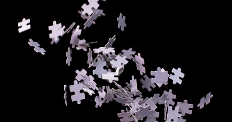 White puzzle pieces falling down whirling in slow motion on a black background