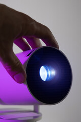 Vertical photo of man's hand adjusting of lens modern wi-fi video-projector with lighting blue light. Video or photo presentation and home movie watching.